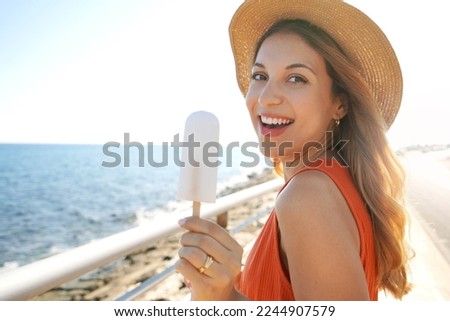 Close-up of laughing Brazilian woman eating a lemon popsicle looking at the camera on summer