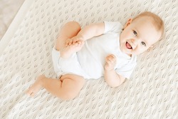 Gros Plan Sur Un Lit En Coton Blanc, Un Bébé Joyeux Et Riant Dans Une Chambre Lumineuse, Un Petit Garçon Ou Une Fille Souriant Allongé Sur Son Dos