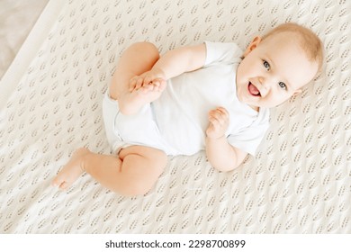 close-up of a laughing happy baby on a white cotton bed in a bright bedroom, a small smiling baby boy or girl lying on her back - Shutterstock ID 2298700899
