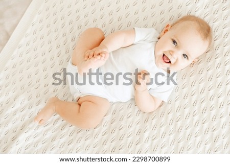 close-up of a laughing happy baby on a white cotton bed in a bright bedroom, a small smiling baby boy or girl lying on her back