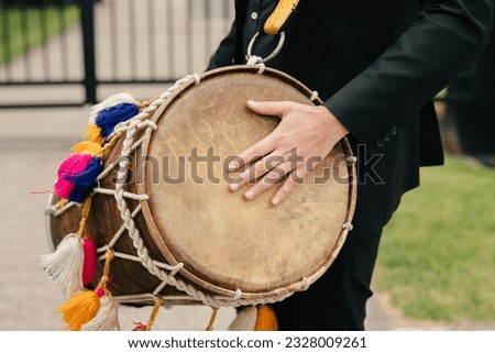 Close-up of a leather drum on a musician's neck. A street musician with a musical instrument in the form of a drum plays a rhythm. Festive musical accompaniment in the form of a rhythm on a drum