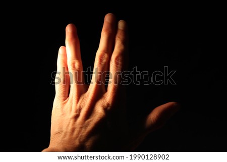 Closeup of left hand back side raised making sci fi salutation gesture isolated on black background. Thumb extended while the fingers are parted between the middle and ring finger. Selective focus.