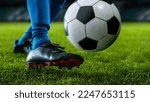 Close-up of a Leg in a Boot Kicking Football Ball. Professional Soccer Player Hits Ball with Fierce Power and Scores Goal, Grass Flying. Beautiful Cinematic Low Angle Ground Artistic Shot