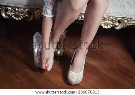 closeup leg caption of model girl wearing white dress sitting on victorian sofa using left shoe holding  hand over right toes