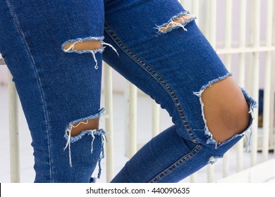 Close-up legs of Asian woman standing wearing torn jeans worn with a prison cell.