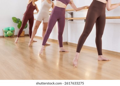 Primer plano de las piernas en una clase de fitness de ballet barre. Mujeres irreconocibles en colorida postura activa de trabajo y equilibrio en un estudio brillante con pisos de madera. Control de entrenamiento funcional. Copiar espacio