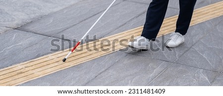 Close-up of the legs of a blind businesswoman walking along a tactile tile with a cane. Widescreen. 
