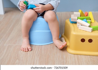 Closeup of legs of cute little Asian 18 months old toddler baby boy child sitting on potty playing with wooden blocks toy. Kid playing with educational toy & Toilet training concept. - Selective focus