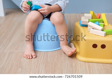 Closeup of legs of cute little Asian 18 months old toddler baby boy child sitting on potty playing with wooden blocks toy. Kid playing with educational toy & Toilet training concept. - Selective focus