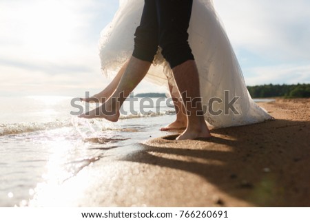 Closeup legs of loving couple on the beach make a splash with their feet, near the sea standing on sand. Side by side on the wet sand, enjoying the waves. Legs couple in love happy couple walks.