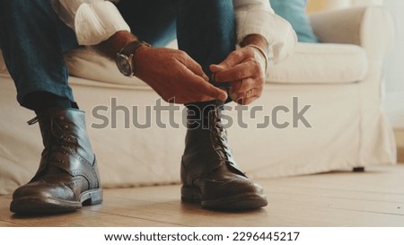 Close-up of legs of mature man putting on casual boots, tying shoelaces