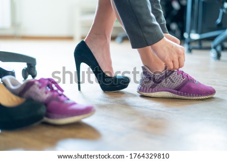Close-up of legs of an office female employee with foot pain. A woman changes high black suede heels to more comfortable shoes. The girl takes off her shoes and puts on purple running shoes.