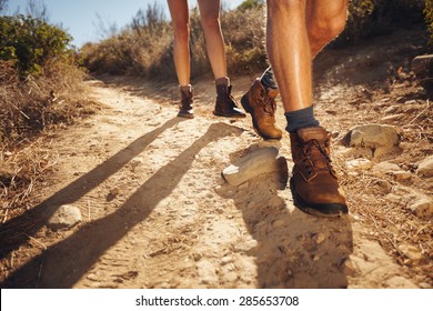 Close-up of legs of young hikers walking on the country path. Young couple trail waking. Focus on hiking shoes.
