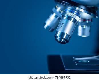 Closeup Lens Of A Modern Microscope In A Research Lab On A Dark Blue Background. High Resolution Studio Image.