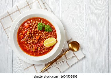 Close-up Of Lentil Soup With Vegetables And Lemon Wedges In A White Bowl On A Wooden Table With A Golden Spoon And Toasts, Horizontal View From Above, Flatlay, Free Space