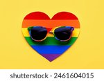 Closeup of LGTBI flag sunglasses on LGTBI heart over yellow background. LGBT Pride concept