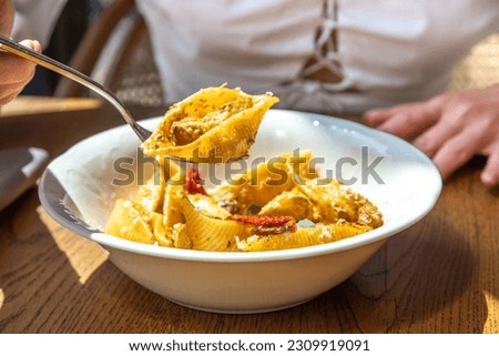 Close-up lifestyle girl in restaurant eat conchiglioni, conchigliette pasta with meat or green vegan meat, with vegetables, on terrace, hands in picture. Healthy italian, Mediterranean lunch