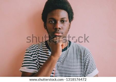 Closeup lifestyle toned portrait of young handsome dark-skinned african american confident man looking at camera on pink wall background. Indoor soft focus portrait of nigerian male in striped shirt.