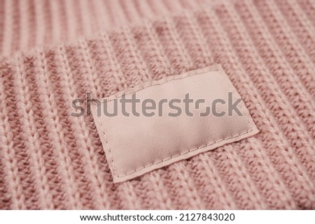 Close-up of a light, pink woolen knitted hat, for a girl. Mock-up, a light-colored empty fabric tag sewn to a headdress for a logo or brand. A uniform. Teen brand, women's accessory