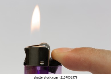 Close-up lighter burn isolated on white background. Transparent purple plastic gas chamber lighter lit by a finger.
