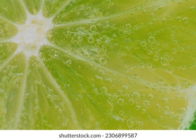 Close-up of a lime slice in liquid with bubbles. Slice of ripe lime in water. Close-up of fresh lime slice covered by bubbles. Macro shot of a slice of lime in sparkling water. Citrus in water.