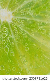 Close-up of a lime slice in liquid with bubbles. Slice of ripe lime in water. Close-up of fresh lime slice covered by bubbles. Macro vertical image