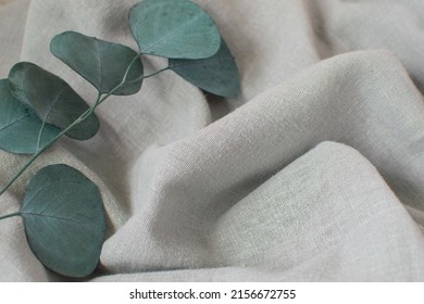 Close-up of a linen fabric with undulating folds and a branch of green eucalyptus. Textile background. Eco-friendly natural materials.harmonious color combination. - Shutterstock ID 2156672755