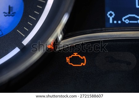 Close-up of a lit orange check engine warning light on the dashboard of a modern car. Selective focus.