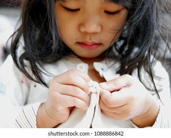 Closeup of little Asian baby girl, 28 months old, trying to button a pajamas by herself - child development by learning to do things by themselves - Powered by Shutterstock