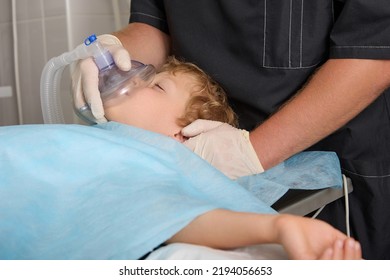 Close-up Of A Little Boy Sleeping In The Intensive Care Unit Under A Ventilation Mask. The Pediatrician Makes Anesthesia To The Child Using An Oxygen Mask For Surgical Treatment Of The Patient