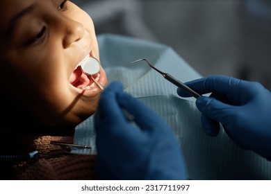 Closeup of little child in teeth checkup at dental clinic, unrecognizable dentist holding tools and mirror, copy space - Powered by Shutterstock