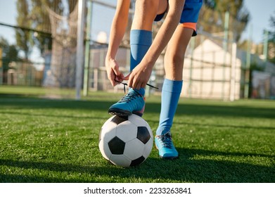 Closeup little football player tying shoelaces putting leg on ball - Powered by Shutterstock