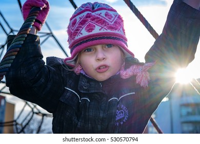 Close-up of a little girl in children's jungle gym. Seven years old. In winter. Front. Sunset. Girls play on the playground equipment in the park. - Powered by Shutterstock