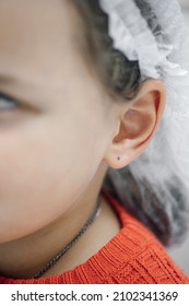 Close-up Of Little Girl Ear With Black Dot From Marker. Preparation For Ear Piercing. Child In Disposable Medical Cap