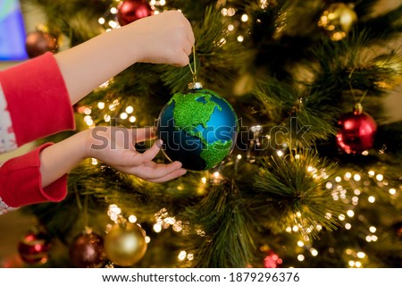 Close-up of little girl hanging Xmas glass bauble decoration ornament globe planet earth on christmas tree.  Merry christmas and new year concept. Selective focus