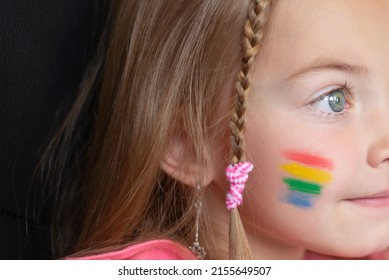 Close-up of a little girl with a rainbow flag painted on her cheeks. Portrait of a child from an LGBTQ family . Pride Day, LGBT family, concepts of rights and equality - Powered by Shutterstock