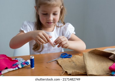 Close-up Of A Little Girl Sewing Things By Herself. Creates A Product With His Own Hands. The Child Is Learning To Sew. Sustainable Development Of The Life Of A Child And An Adult. Conscious And Reusa