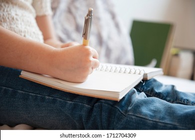 Close-up Of The Little Girl's Hand Writing On Paper Notebook With A Pen. Little Girl Writes In Her Diary Or Draws In Bedroom. Preschoolers Learn To Write Or To Draw. Creativity And Talent. Childhood.