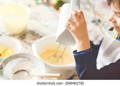 Closeup of little kid boy baking chocolate cake and tasting dough in domestic kitchen, indoors. Close-up of child having fun with working with mixer, flour, eggs dough at home. Little helper