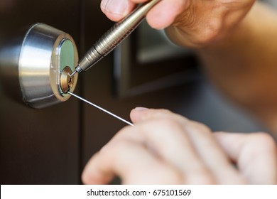 closeup of locksmith hands using pick tools to open locked door