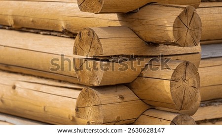 Close-up of a log cabin corner, showcasing the interlocking logs and wood grain texture. Natural light highlights the wood's color and detail.