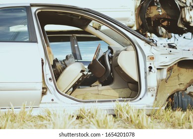 A Closeup Look Of An Abandoned Car Front Without A Door Or Wheel In A Dry Paddy Field After Harvest. More Damaged Vehicles Are Around It.