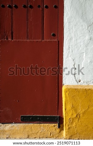 A close-up look at the rustic red door of the Maestranza bullring in Seville, showcasing its historic charm and architectural details.