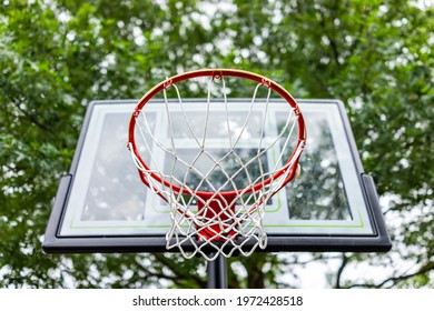 Closeup looking up under red basketball hoop with net and glass board in playground looking up at sky and house in background