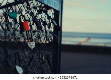 A close-up of love locks attached to a metal fence, symbolizing eternal love. The background fades into a soft focus, revealing a seaside view with gentle waves, adding to the romantic atmosphere. - Powered by Shutterstock