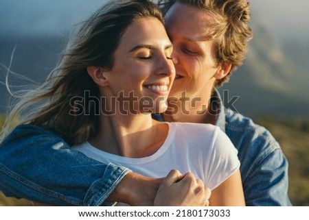 Close-up of loving caucasian young man cuddling and romancing with happy beautiful girlfriend during outing at sunset