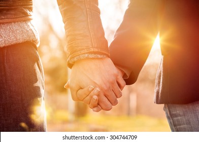 Closeup of loving couple holding hands while walking at sunset