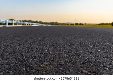Close-up low angle view of asphalt road with guardrail and green fields at sunset, symbolizing journey, travel, and freedom