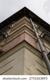 Close-up low angle view of the corner of a traditional residential building featuring red bricks, balconies, and a long vertical drainpipe.