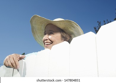 Closeup Low Angle View Of A Smiling Woman Peering Over Garden Fence